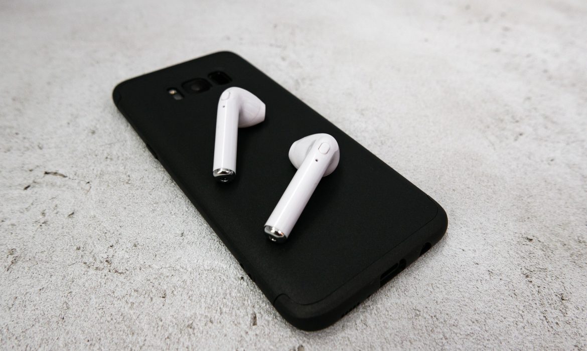 Close-up of white earbuds on black mobile phone. Wireless earbuds, earphones.