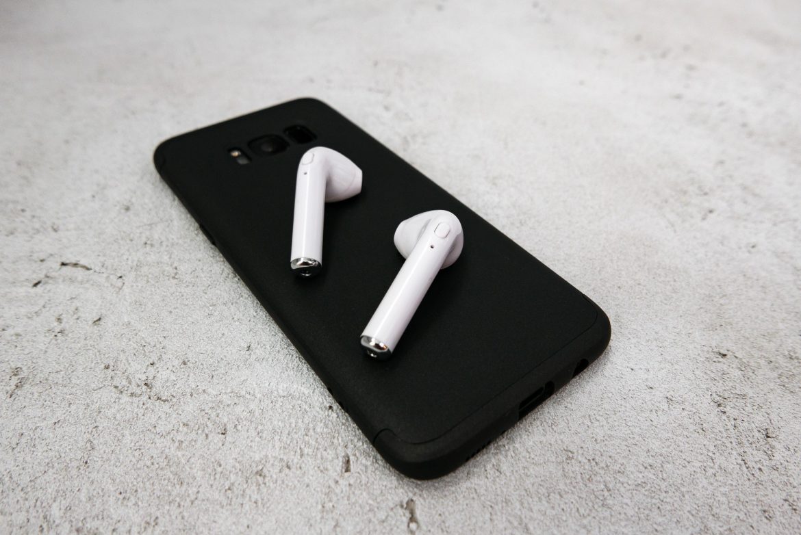 Close-up of white earbuds on black mobile phone. Wireless earbuds, earphones.